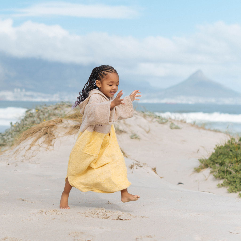 Kid running on the beach in mahina changing towel/ surf poncho, with table mountain in the background
